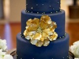 a navy and gold wedding cake decorated with a sugar flower and beads