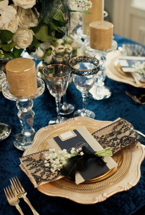 a navy, gold and white tablescape, candles, gold rim glasses and a setting with lace