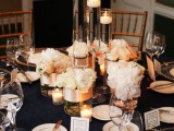 a chic navy, gold and creamy wedding tablescape with candles, white floral centerpieces and a sheer charger