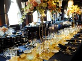 a navy and gold wedding table setting with lush floral centerpieces, sheer chargers, gold candle holders