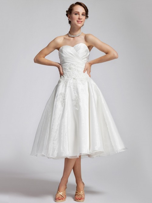 a strapless A-line tea length with a draped bodice, some lace appliques and a pleated skirt, shiny shoes and a statement necklace