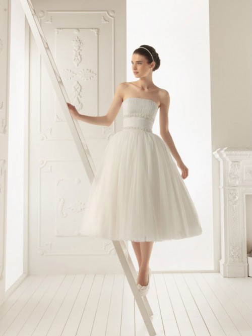 a strapless A-line tea length wedding dress with a pleated bodice, a wide sash and a pleated skirt, white shoes and a headband