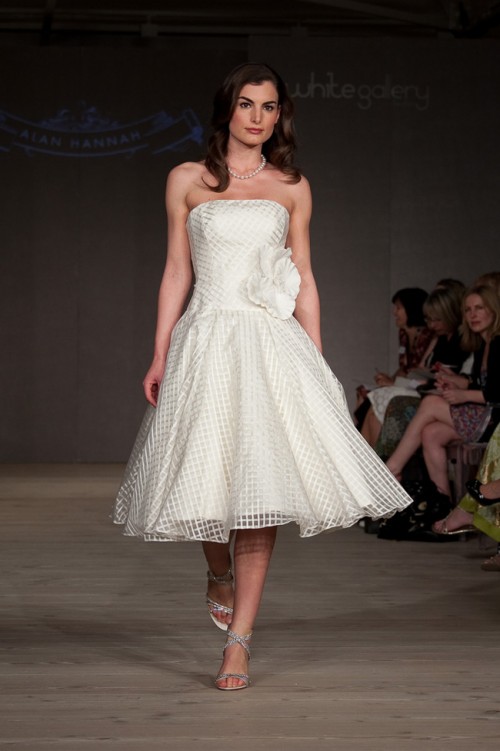 a strapless A-line tea length wedding dress with a large fabric bloom, silver shoes and a pearl necklace is very chic