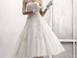 a strapless a-line wedding dress with lace appliques and embellishments, with gloves, a veil with a fabric bloom and white shoes with bows