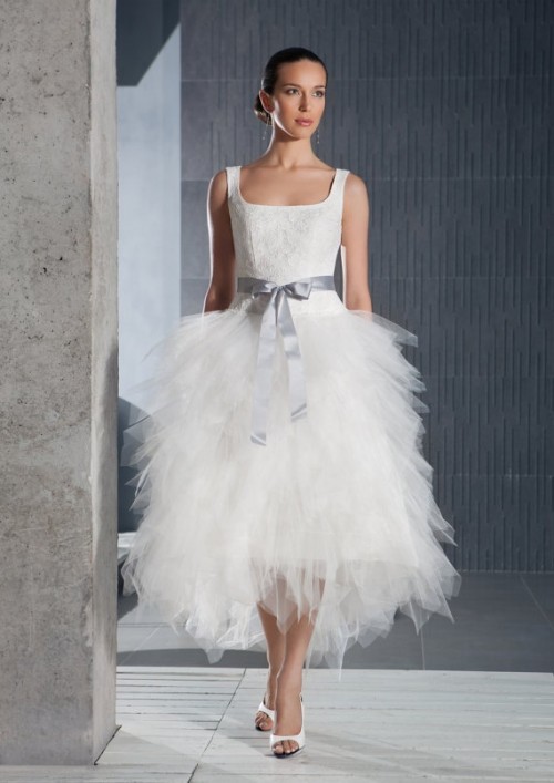 a tea length wedding dress with a lace bodice and a ruffle tulle skirt, a grey sash and white shoes for a modern playful look