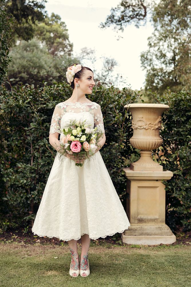 A lace A line tea length wedding dress with an illusion neckline and short sleeves, white shoes and a blush fabric headpiece