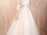 a nude and white lace tea length wedding dress with long sleeves, a V-neckline and a pleated skirt plus white shoes