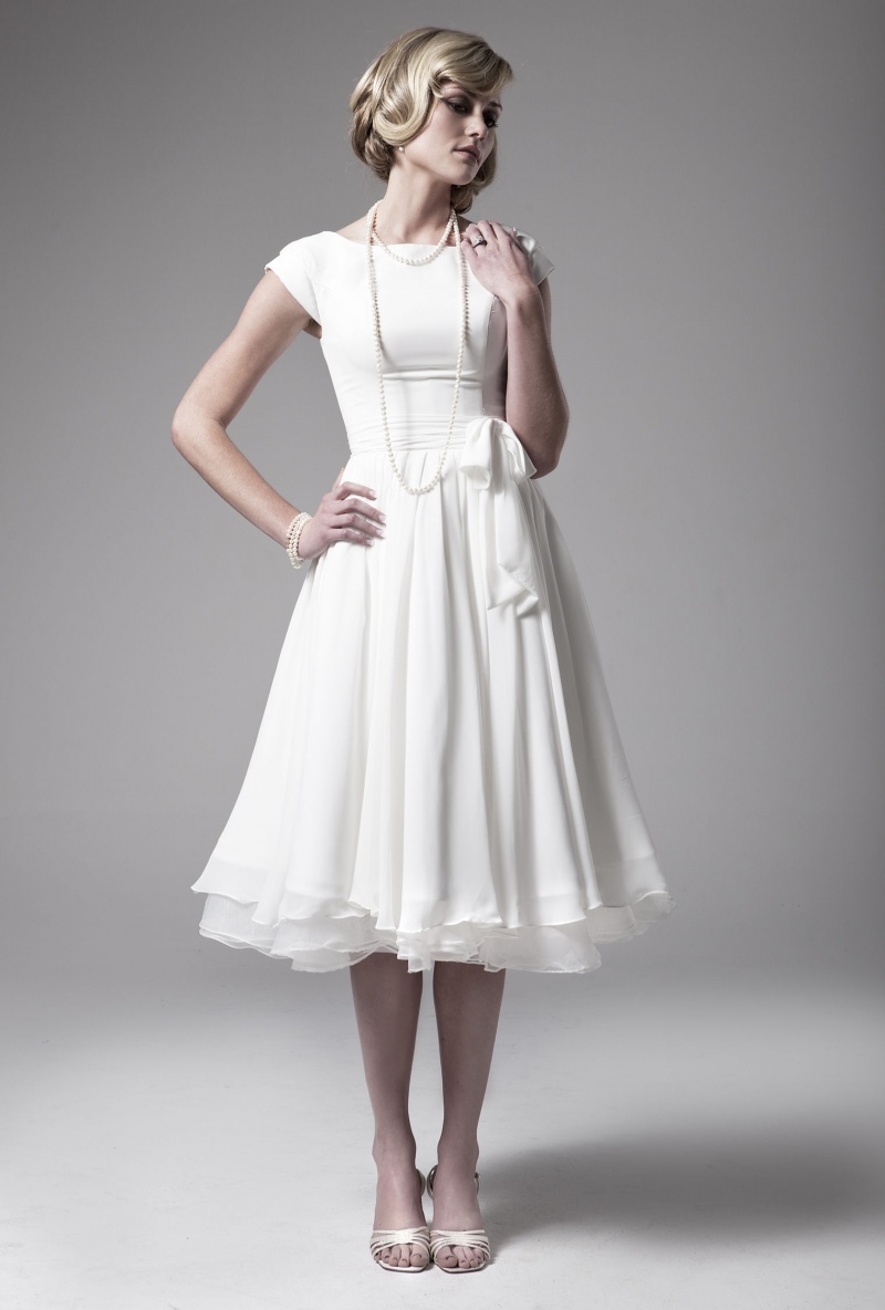 A plain A line tea length wedding dress with a high neckline, cap sleeves and a pleated skirt plus vintage shoes and a strand of pearls for a vintage look