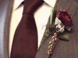 a moody vintage wedding boutonniere of a dark burgundy bloom, berries and pale leaves is a lovely accessory for a fall wedding