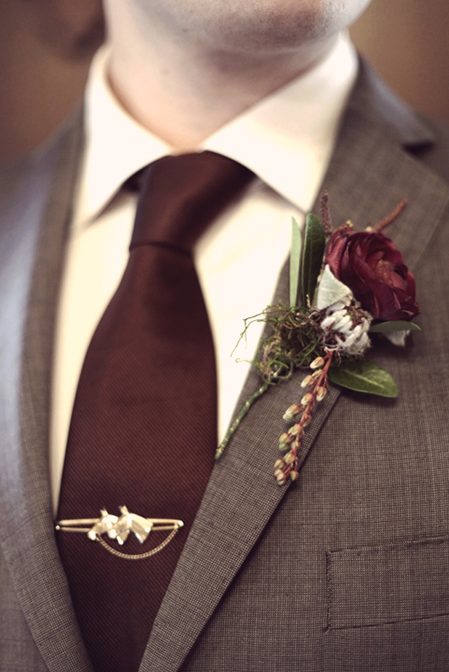 a moody vintage wedding boutonniere of a dark burgundy bloom, berries and pale leaves is a lovely accessory for a fall wedding