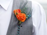 a catchy wedding boutonniere of orange roses, feathers and a wrap is a stylish touch of color to the groom’s look