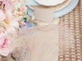 elegant beach bridal shower decor with a wicker table runner, blue and tan plates, corals and pink blooms