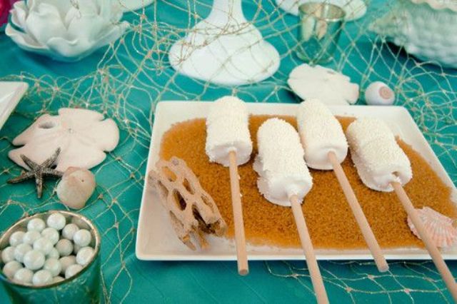 A beach bridal shower dessert table with marshmallow pops, candies, net and seashells