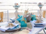 a bright beach bridal shower tablescape done with touches of blue, turquoise, neutral linens, candles and lots of seashells