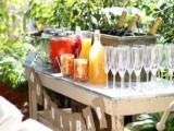 an outdoor bar with a wooden table, glasses, lemonades, drinks and some champagne bottles