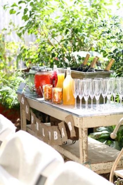 an outdoor bar with a wooden table, glasses, lemonades, drinks and some champagne bottles
