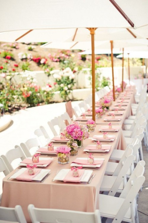 a chic and elegant summer bridal shower tablescape done in pink, with a pink tablecloth, blooms and napkins and umbrellas overhead