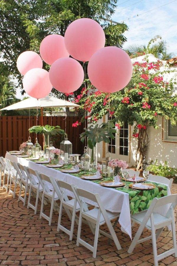 a backyard garden summer bridal shower tablescape done with a bright tablecloth, tropical leaves, pink balloons, candle lanterns