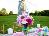 a super colorful bridal shower tablescape with bold linens, blooms and decor and some candles styled right outdoors