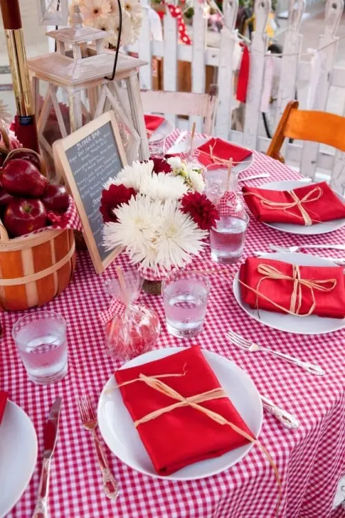 a bright summer bridal shower tablescape with plaid and solid linens, white and red blooms, an apple centerpiece