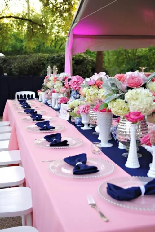 a bold pink and navy tablescape with pink and neutral blooms, navy textiles, a pink tablecloth and white and silver vases