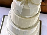 a glam white wedding cake with plain and striped tiers, with rhinestones and an oversized bow on top