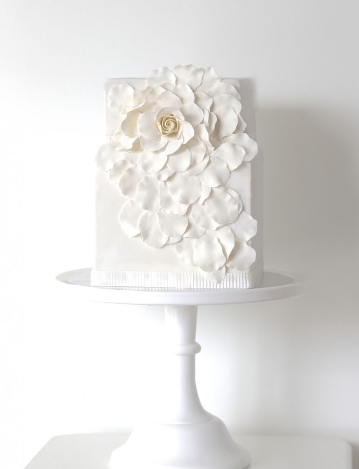 A square wedding cake decorated with a large whiet sugar bloom and petals is a lovely and chic idea