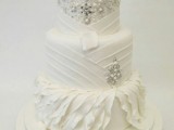 a white wedding cake with patterns, embellishments, pearls and a a white bloom on top