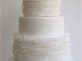a white wedding cake with ruffle and plain tiers, a white sugar bloom on top is a chic and stylish dessert to rock