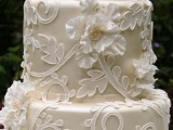 a tan wedding cake with white floral patterns and leaves, with white sugar blooms is a nice fit for a refined wedding