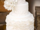 a refined white patterned wedding cake with floral and ruffles patterns and oversized white sugar blooms on top