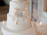 an elegant white wedding cake decorated with edible bows and rhinestones is a very chic and refined piece