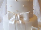 a pure white wedding cake decorated with edible beads, a large bow and sugar blooms on top is a very refined piece