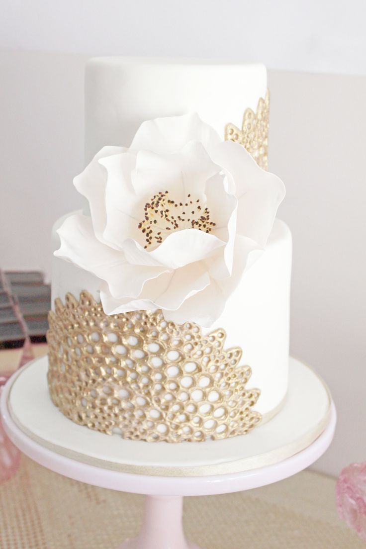 A white wedding cake with gold detailing and an oversized white sugar bloom looks very chic and statement like