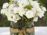 jars with white blooms and greenery and a gold ribbon is a stylish rustic centerpiece for a pretty wedding tablescape