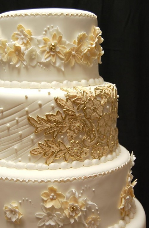 a beautiful wedding cake in white and gold, with edible flowers, pearls, beads, textures and other stuff