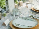 a stylish wedding tablescape with white blooms and greenery, with gold chargers and cutlery and white linens