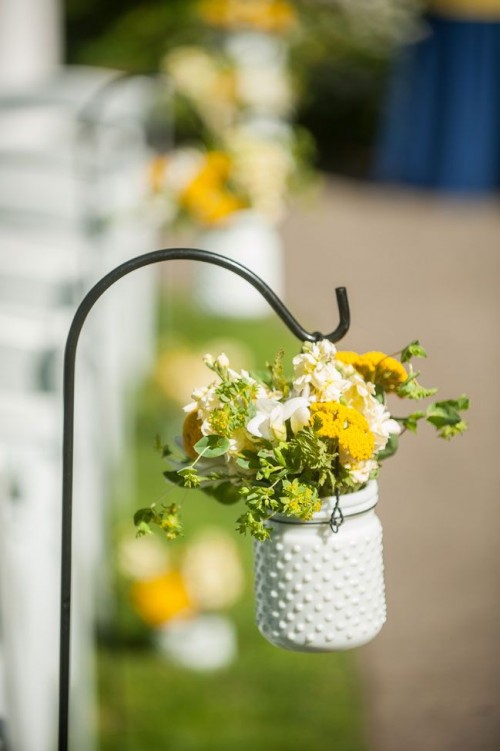 a white milk jar with yellow and white blooms and greenery is a pretty solution for a bright spring or summer wedding