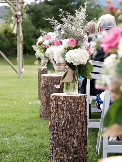 a rustic spring wedding aisle with tree stumps and jars with pink, white blooms and greenery and a bit of burlap is a lovely idea for a rustic spring wedding