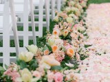 a beautiful and lush spring wedding aisle with pink petals on the ground and pink and peachy bloom arrangements lining up the aisle is amazing