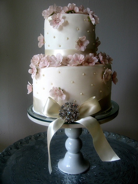 a white buttercream polka dot wedding cake decorated with pink cherry blossom and a vintage brooch and a bow