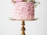 a pale pink textural buttercream wedding cake topped with greenery and some pink blooms is a pretty and delicate dessert for a spring wedding