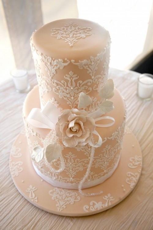 a vintage tan wedding cake with white lace detailing and some bows plus a large sugar bloom is an elegant vintage idea