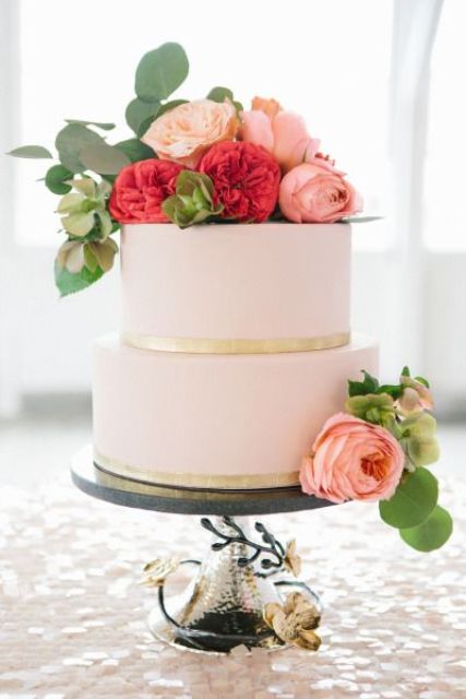 a blush buttercream wedding cake with gold ribbons and pink, red and green blooms plus foliage is a beautiful and chic idea for spring or summer