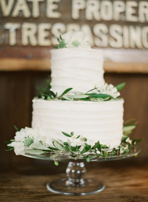 a white textural buttercream wedding cake topped with fresh greenery and white blooms is a chic spring wedding dessert idea