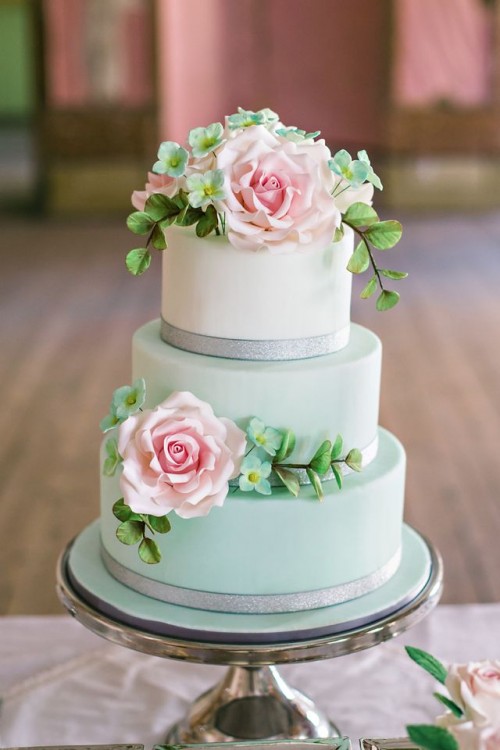 a pastel green and white wedding cake with silver ribbons, blush natural and white faux blooms and greenery for a spring celebration