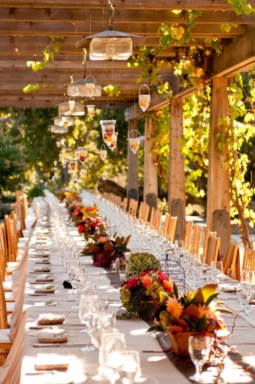 a bold fall vineyard wedding reception with greenery, bold blooms, white linens and catchy yet simple pendant lamps over the table