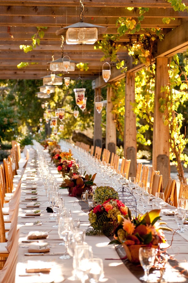 A bold fall vineyard wedding reception with greenery, bold blooms, white linens and catchy yet simple pendant lamps over the table