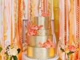 a shiny glam gold wedding cake with coral sugar blooms is a nice idea for a modern bright wedding