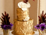 a gold textural wedding cake with sugar blooms and feathers on top for a chic and non-typical wedding dessert table